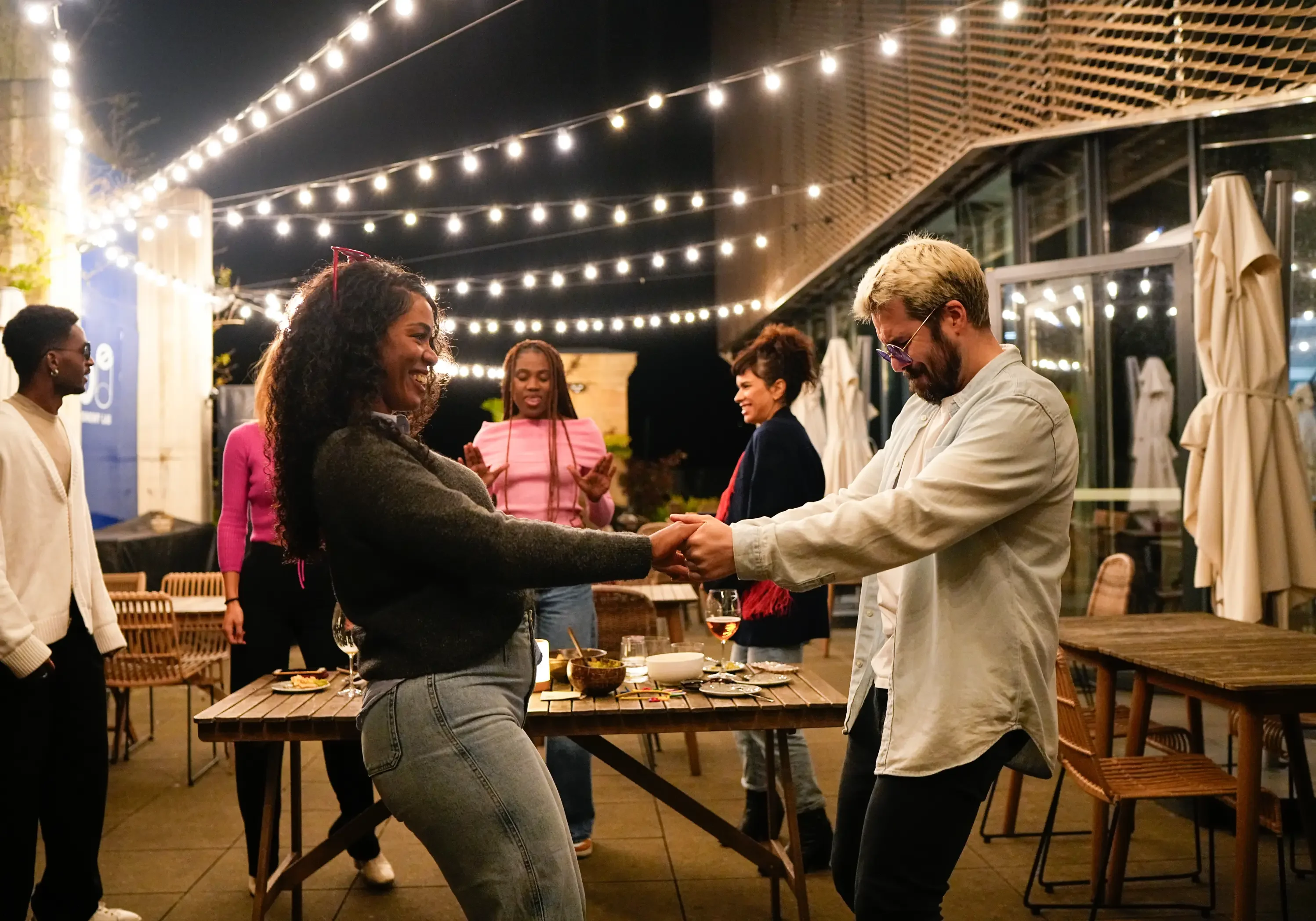 Friends enjoying an outdoor evening party with string lights.